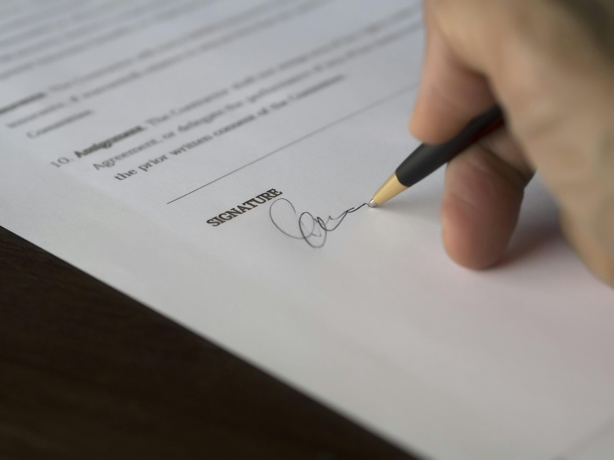 pexels photo 261621 261621 A hand signs a formal contract with a pen on a wooden desk.
