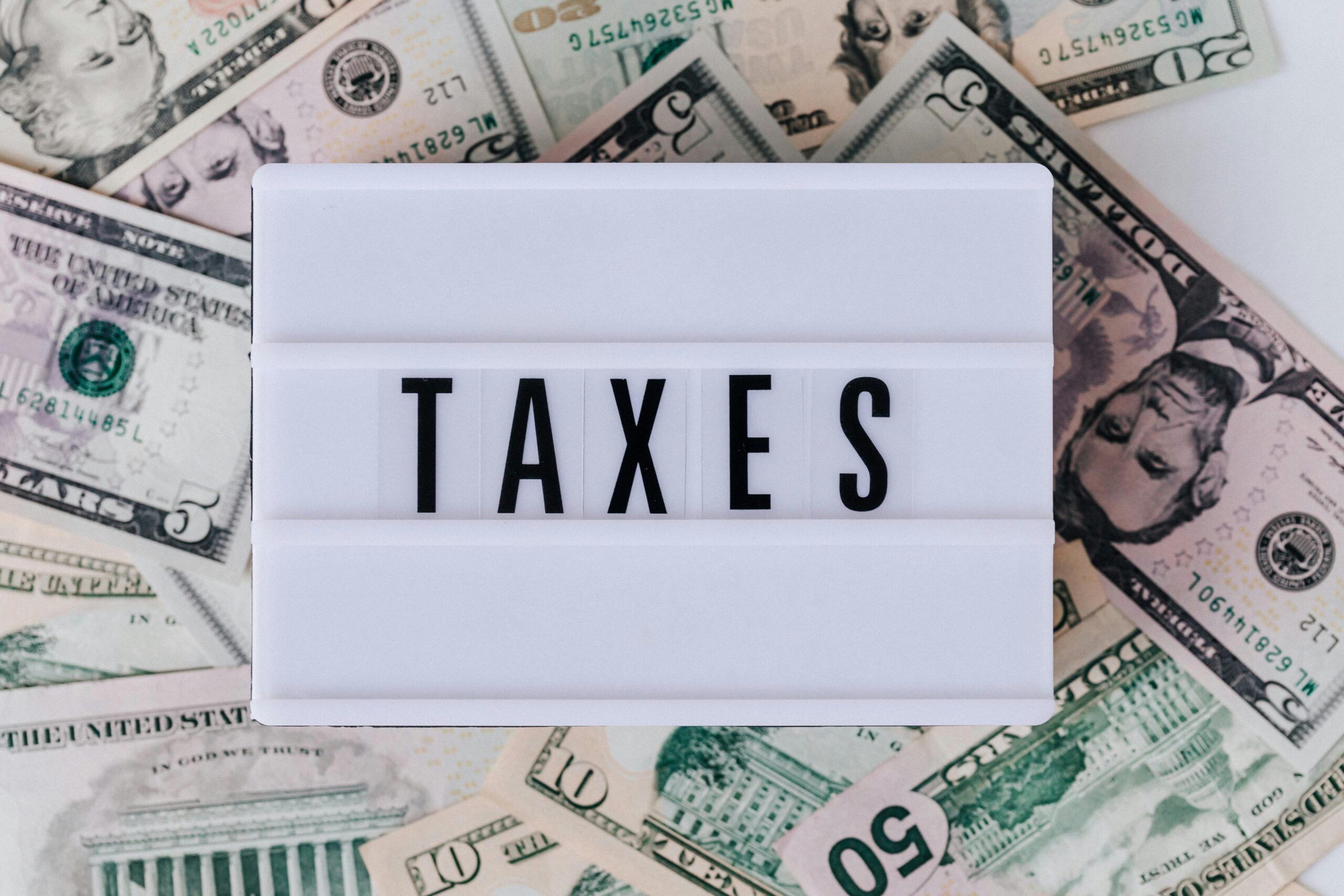 pexels photo 4386372 4386372 Top view of white vintage light box with TAXES inscription placed on stack of USA dollar bills on white surface